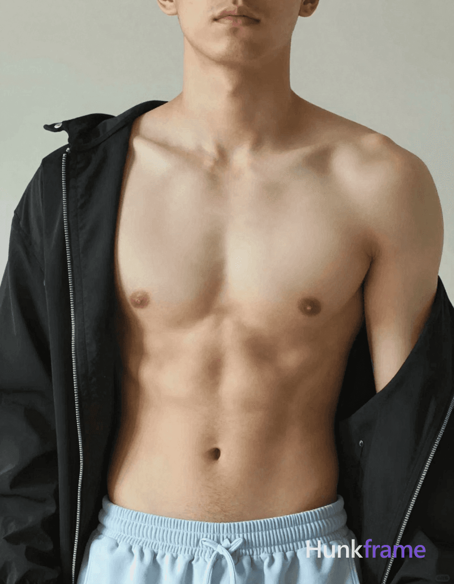 A shirtless man standing with his head slightly tilted forward, wearing a black jacket draped over h