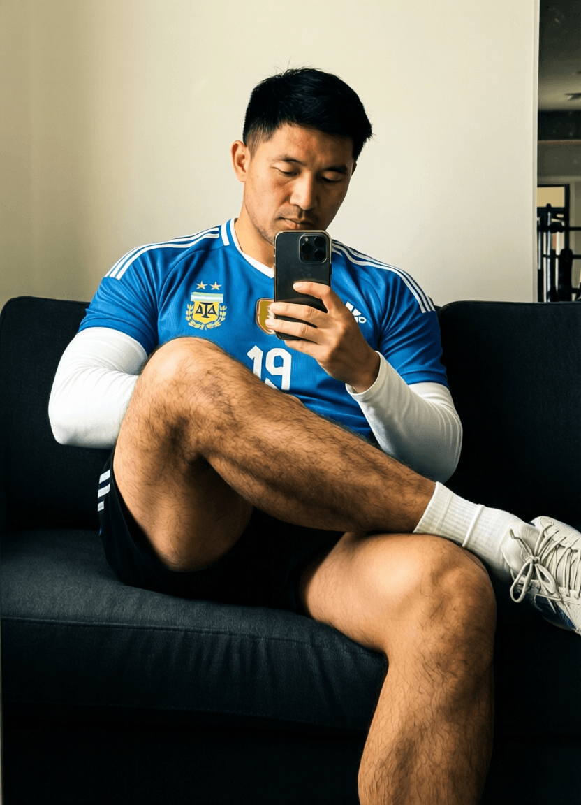 Asian man with light-medium skin and black short styled hair sits on a dark sofa, wearing an Adi
